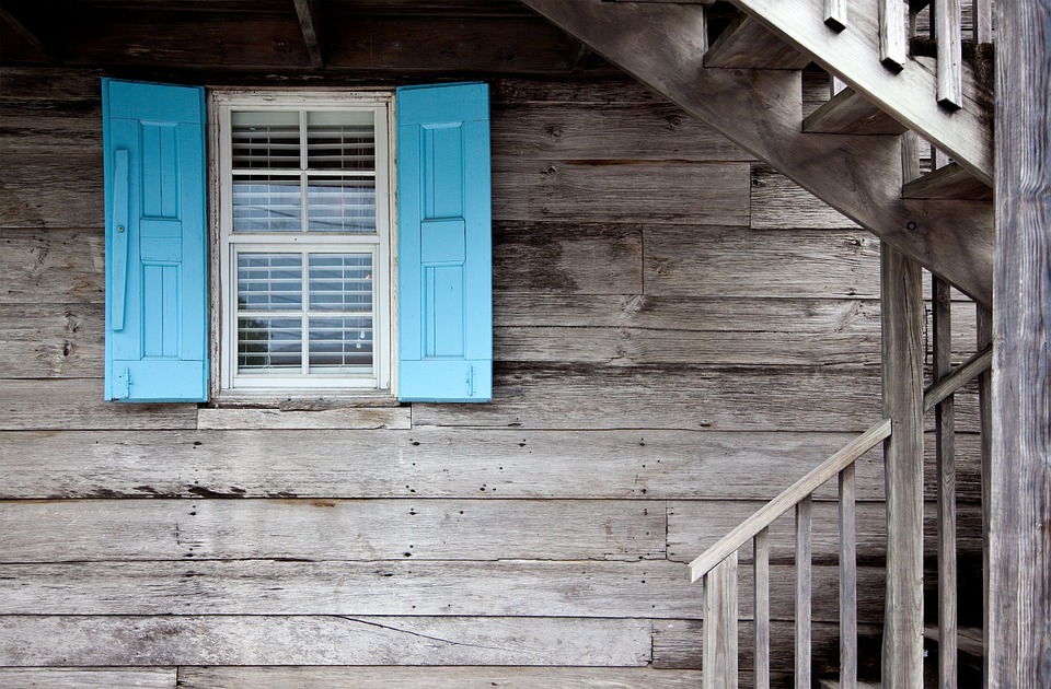 Dēļu apšuvuma ēkas fasādes elements ar logu un zilas krāsas slēģiem